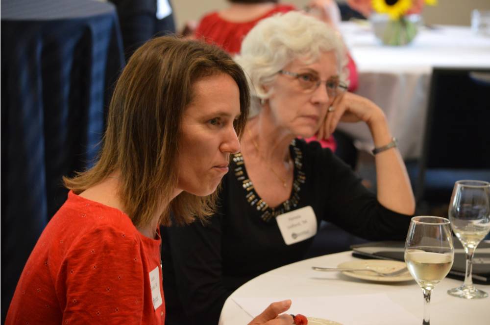 Two alumnae listening to a conversation at a table